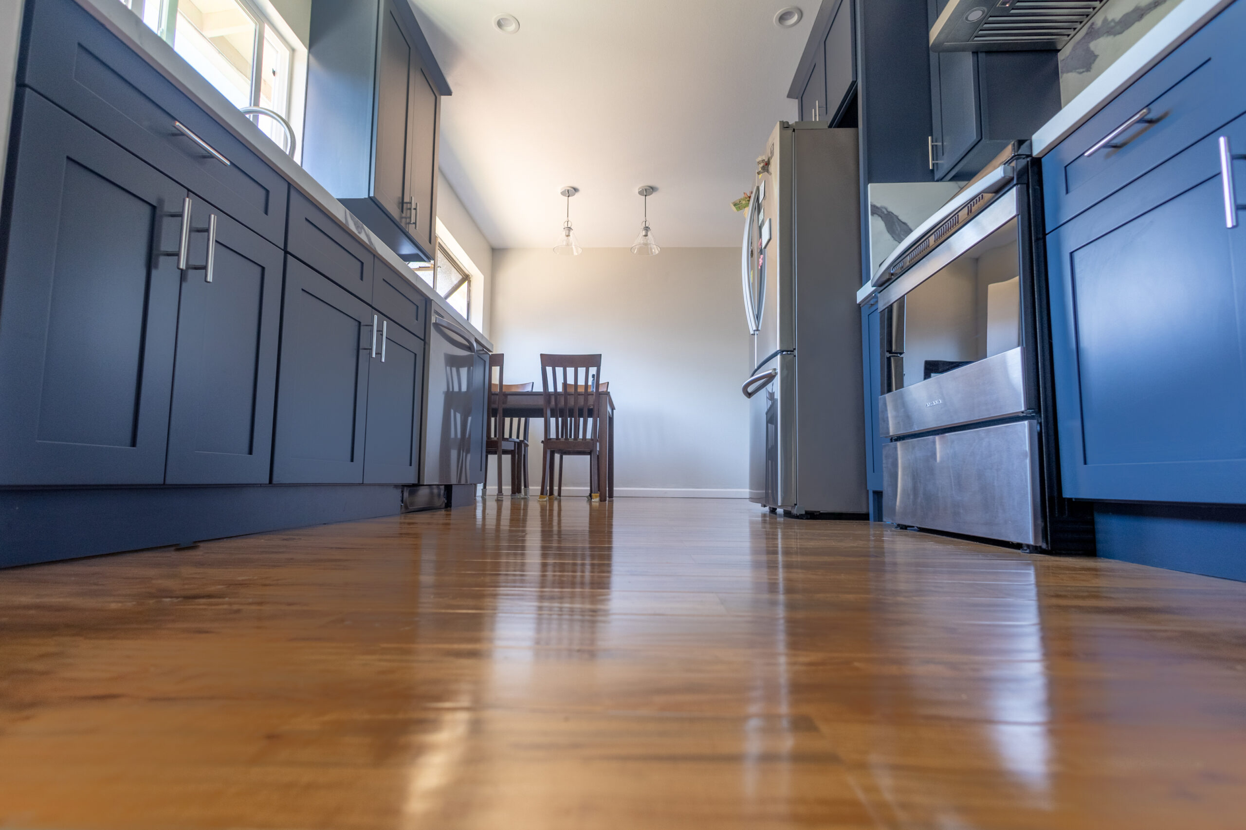 Wide kitchen remodel showing dark blue cabinetry, hardwood flooring, and stainless steel appliances in newly constructed layout.