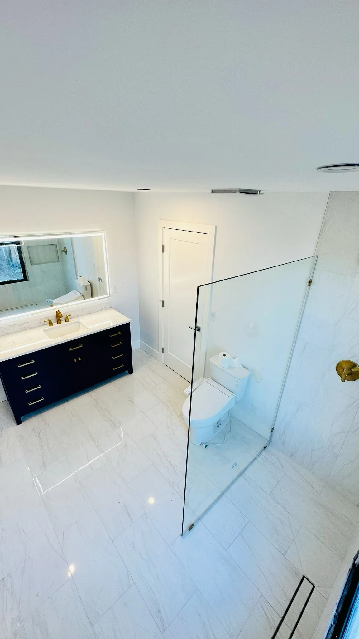 Modern bathroom with black vanity, white countertop, large mirror, and walk-in shower with glass enclosure.