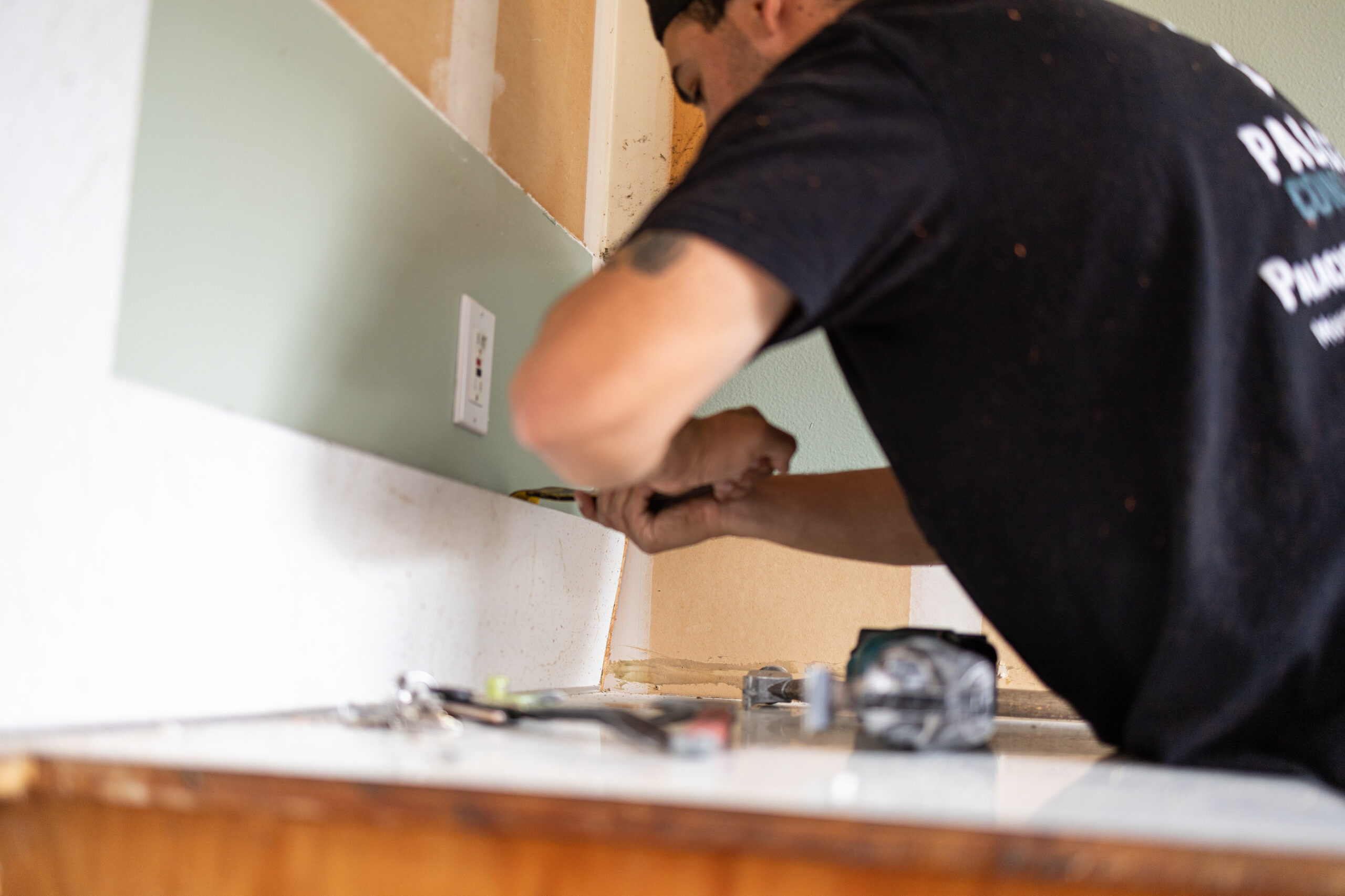 Construction worker cutting drywall during interior wall finishing, representing mid-project remodel work and unexpected costs.